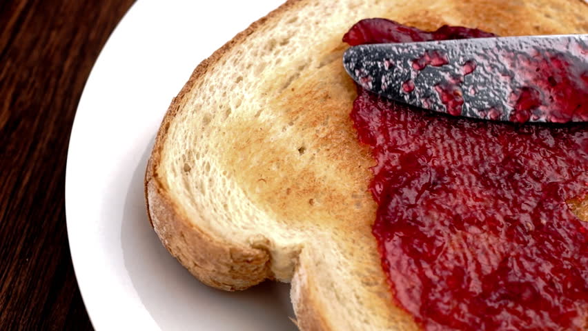 Berry jam being spread on a piece of toast with a knife